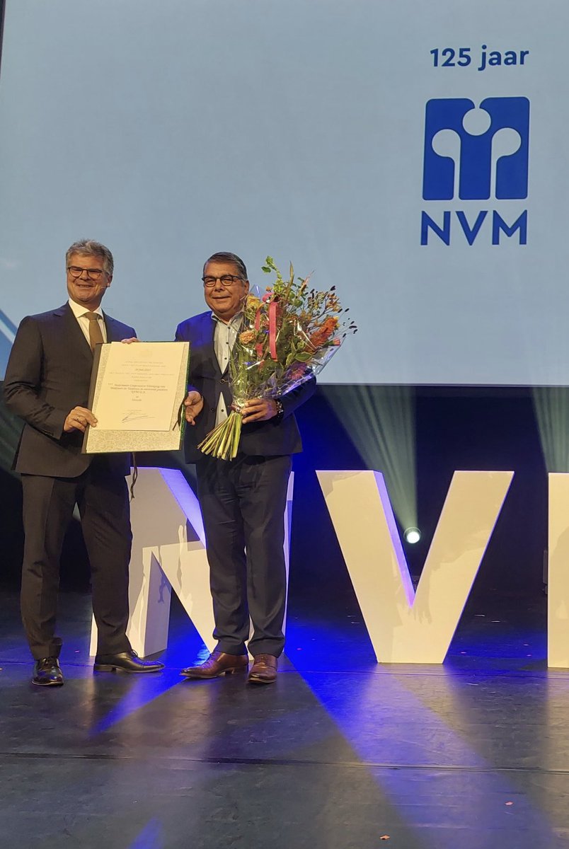 CvdK <a href="/HansOosters/">Hans Oosters</a> overhandigt ‘t predicaat Koninklijk aan dhr Brussel van NVM tijdens de viering van het 125-jarig bestaan. “De NVM heeft een elementaire rol vervuld in de ontwikkeling van het vak, de beroepsethiek en de maatschappelijk toegevoegde waarde,” aldus de commissaris.