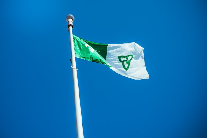 Un mât avec le drapeau francoontarien flottant dans un ciel bleu clair.