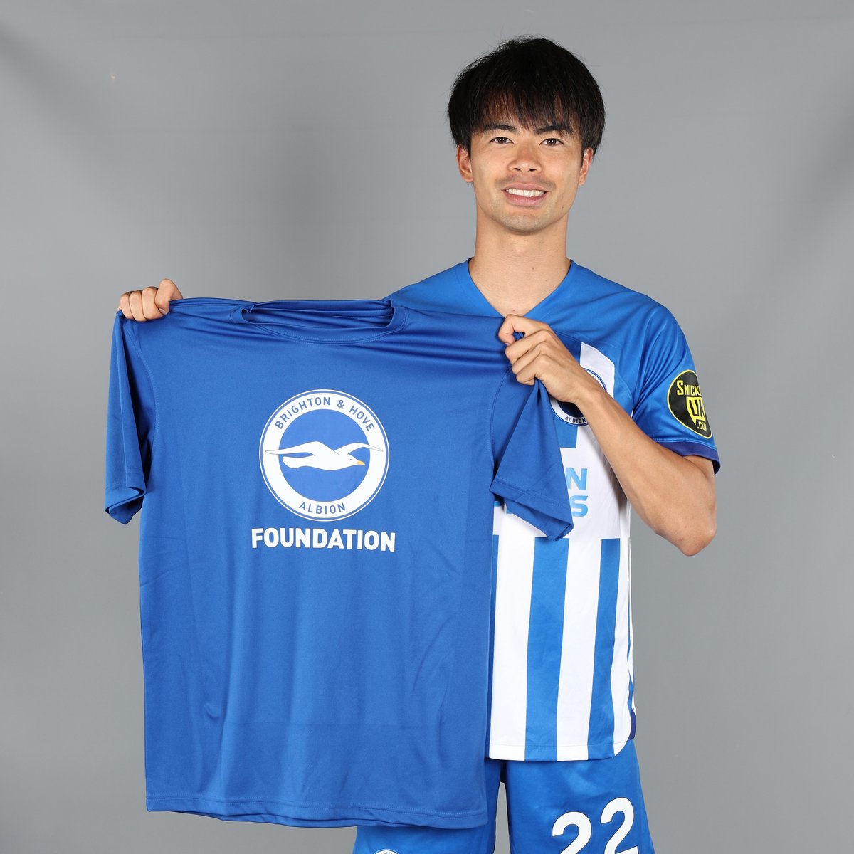 Kaoru Mitoma holding up a 'BHAFC Foundation' t-shirt.