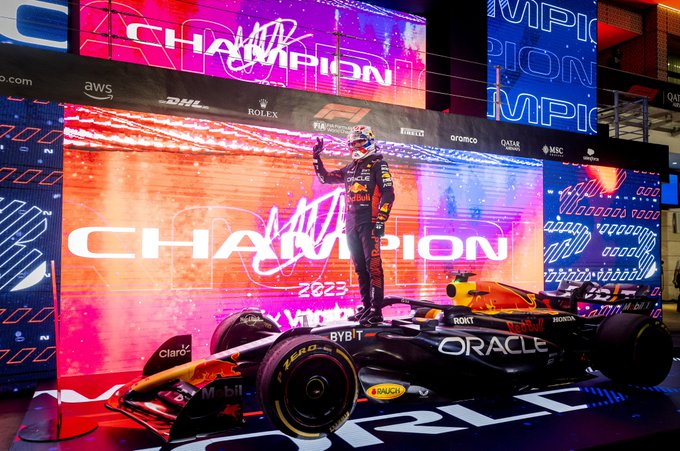 Max Verstappen stands atop his car in parc ferme with plenty of champion motifs in the background, holding up his thumb, index and middle fingers to denote his third world title