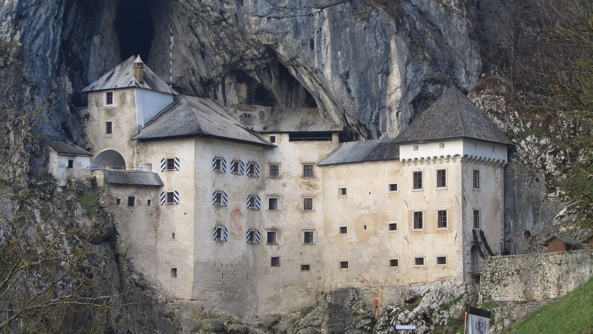 AliciaMimundo's tweet photo. El Castillo de Predjama está construido dentro de una cueva sobre un precipicio de 123 m, en el sudoeste de Eslovenia.

Su construcción actual data de 1570 por encargo de Ivan Kobenzl.  Rodeado de leyendas, la cueva cuenta con innumerables pasadizos y túneles. 
De entre las leyendas destacar la del “Robin Hood esloveno”, de nombre Erasmo. Pues bien, a mediados del s. XV el emperador Federico III de Habsburgo y el rey Matthias Corvinus de Hungría estaban en guerra y Erasmo apoyaba a Corvinus. 
En el devenir de la contienda, Federico III ordenó decapitar injustamente a un amigo de Erasmo. Éste, hizo lo propio por venganza, y mató a un pariente del emperador. La ira imperial no se hizo esperar, ordenó encontrarlo y matarlo. Erasmo hubo de escapar, encontrando en Predjama el lugar perfecto para refugiarse.

Durante un año y un día el castillo de Predjama fue asediado sin éxito. Y mientras, nuestro “Robin Hood”, asaltaba las caravanas de comerciantes del emperador, se abastecía de bienes saliendo y entrando por la cueva del castillo y desesperando a los sitiadores que no veían cómo poder terminar con él. 
Y hete aquí que aparece el traidor de toda leyenda. Así es, un criado de éste lo delató y fue descubierto mediante un ardid. En el momento en el que el caballero, por necesidades fisiológicas fue al baño, el felón encendió una luz señalando su posición al ejército que disparó varios cañonazos acabando con su vida al momento. 
Ahí se puso fin a la historia de Erasmo de Predjama, el “Robin Hood esloveno”. 
Hay quien dice que está enterrado en lo que hoy es el aparcamiento. ¿Quién sabe?
