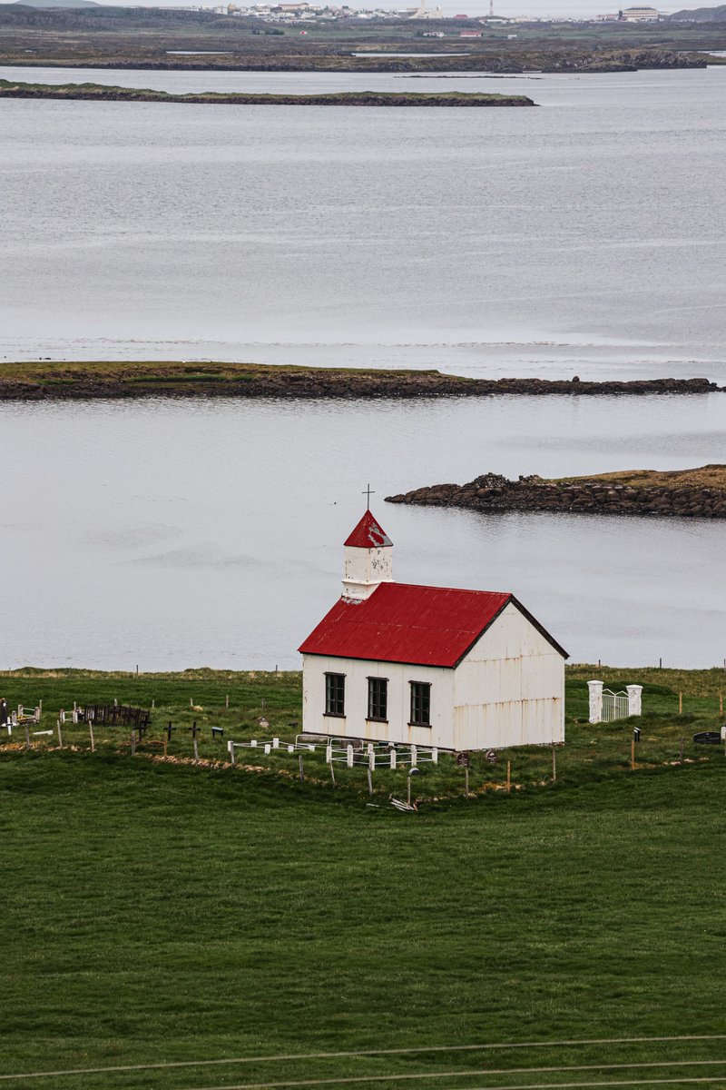 Where serenity meets sanctity - a red-roofed church nestled by the tranquil Icelandic lake. Each view is a silent sonnet of nature's grace. Have you experienced this peaceful embrace? 🏞️🏰