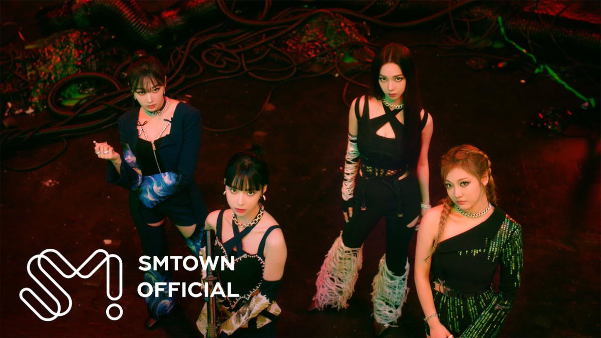 A promotional image showing four women in edgy black outfits in a dark setting with red lighting, featuring the 'SMTOWN OFFICIAL' logo in the bottom left corner.