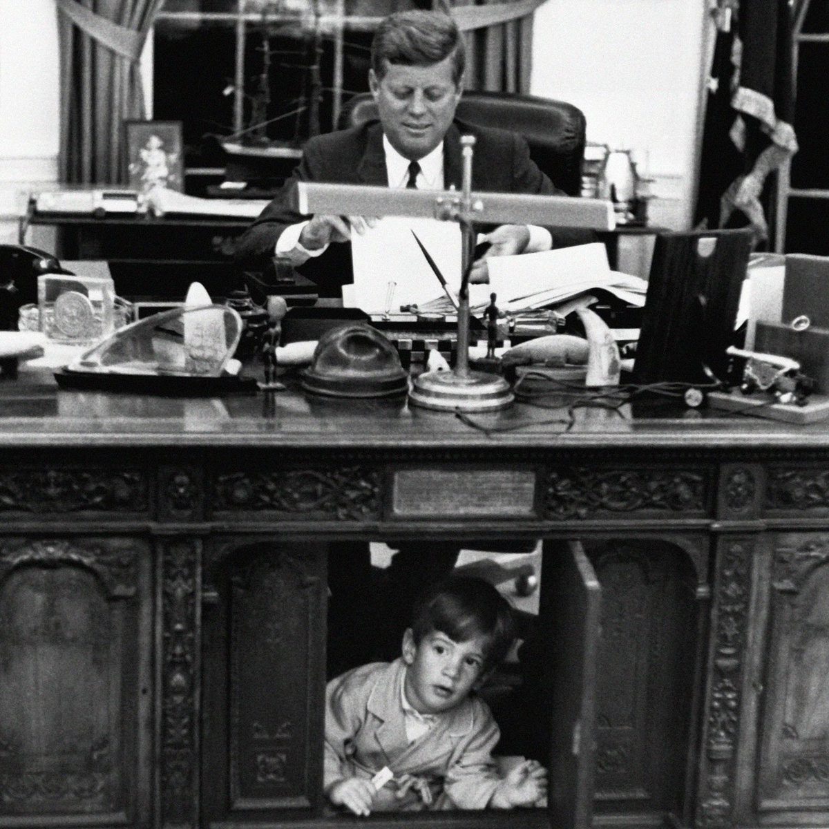 Esta es una de las fotografías más conocidas del presidente americano John F. Kennedy (JFK).

En ella se le vé en el Despacho Oval trabajando, mientras su hijo John John trastea por el suelo.

Pero esa foto tiene un detalle poco conocido.

Fijáos bien sobre la mesa...