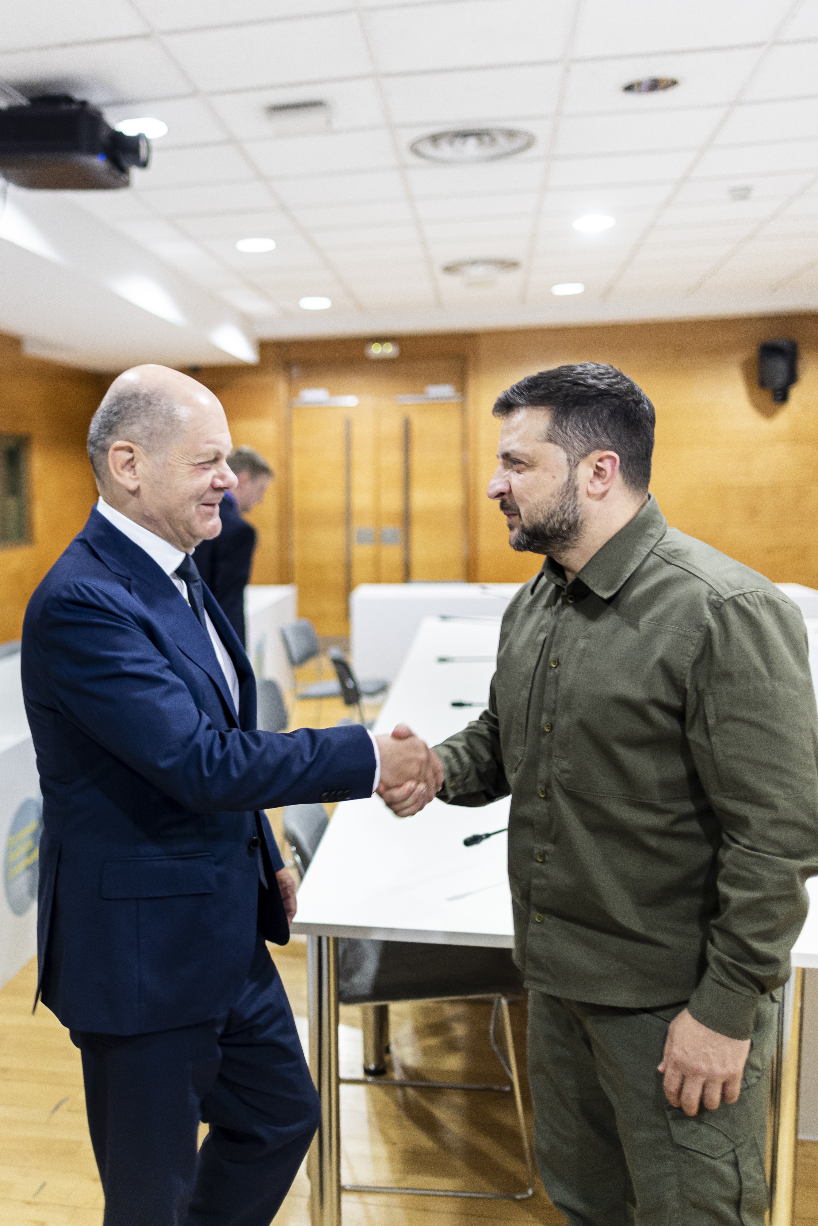 Das Foto zeigt Bundeskanzler Olaf Scholz bei der Begrüßung mit einem Händeschütteln des ukrainischen Präsidenten Wolodymyr Selenskyj. 