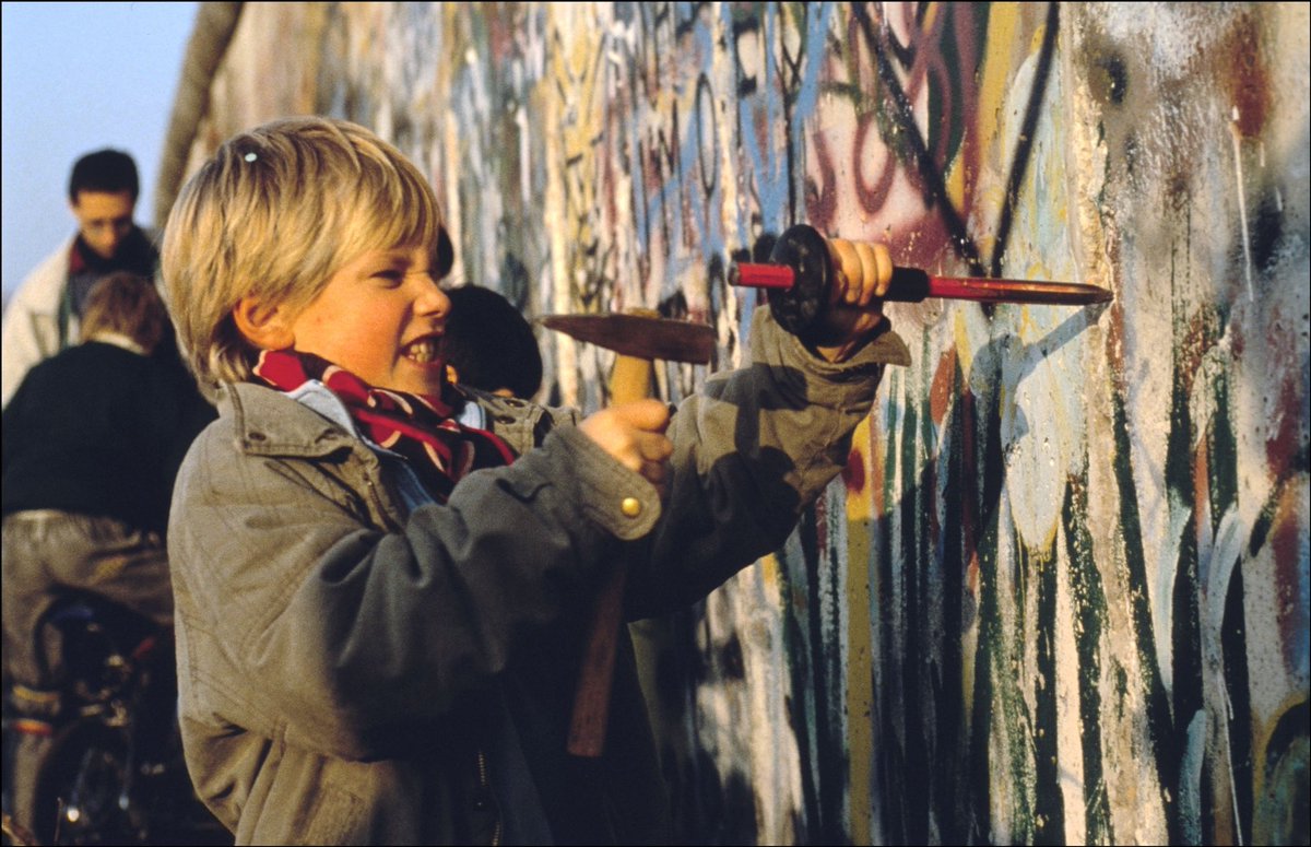 historyinmemes's tweet photo. A child helps to break down the Berlin Wall, 1989.

After standing for 28 years and separating families for a long and painful period, the Berlin Wall finally fell in 1989, allowing East and West Berliners to meet each other. The wall has become an international symbol of death, oppression, and most obviously, it showed the failure of communism.

Due to new reforms in the Soviet Union at the time, the people got the opportunity to break down the wall after being oppressed by East German leader Erich Honecker, who was a hard-line Stalinist. Former president of the Soviet Union, Mikhail Gorbachev, has even claimed to have told a friend that he thought Honecker was "a scumbag." No longer able to withstand the might of the people crowding around the wall, and with Western media filming the event, the gates were opened, and people from both sides began to meet in the middle. Some even brought sledgehammers to break down parts of the wall. This little guy did his part to help, and his face is full of determination!

As John Fitzgerald Kennedy once famously said, "Democracy is not perfect, but we never had to build a wall to keep our people in."