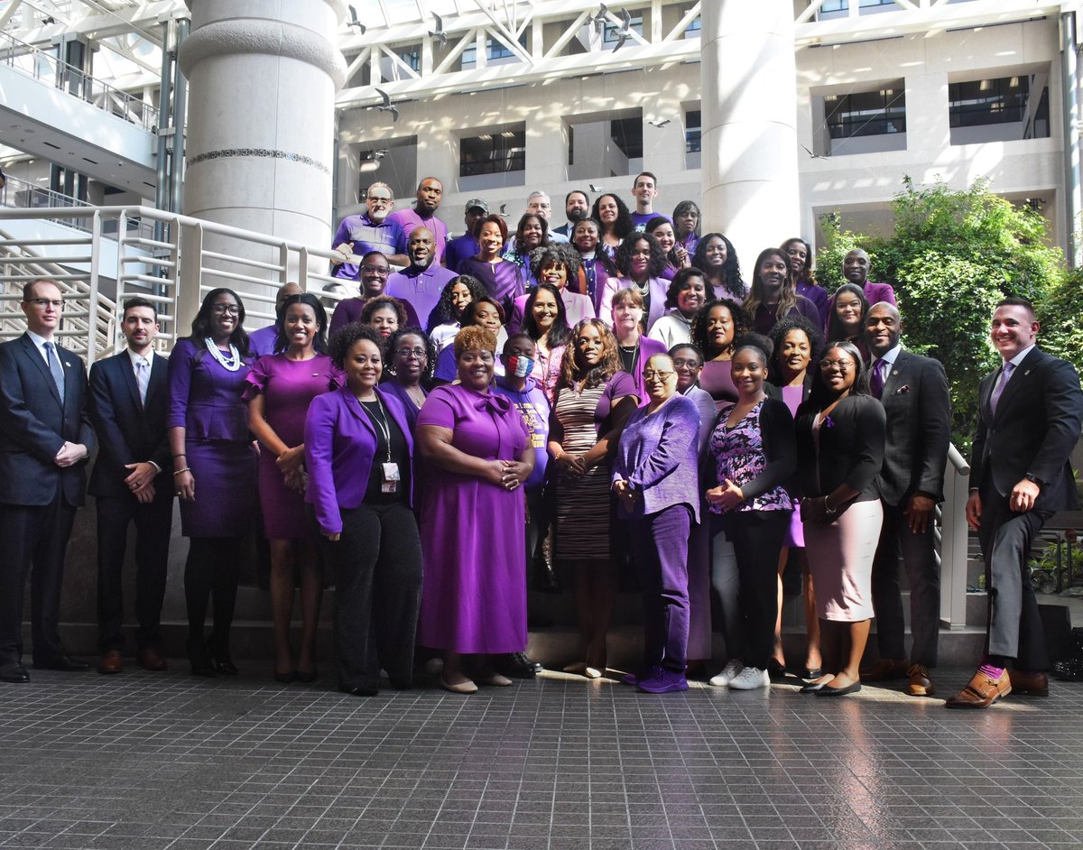 A large group of Fulton County District Attorney’s Office employees standing in an atrium wearing purple outfits