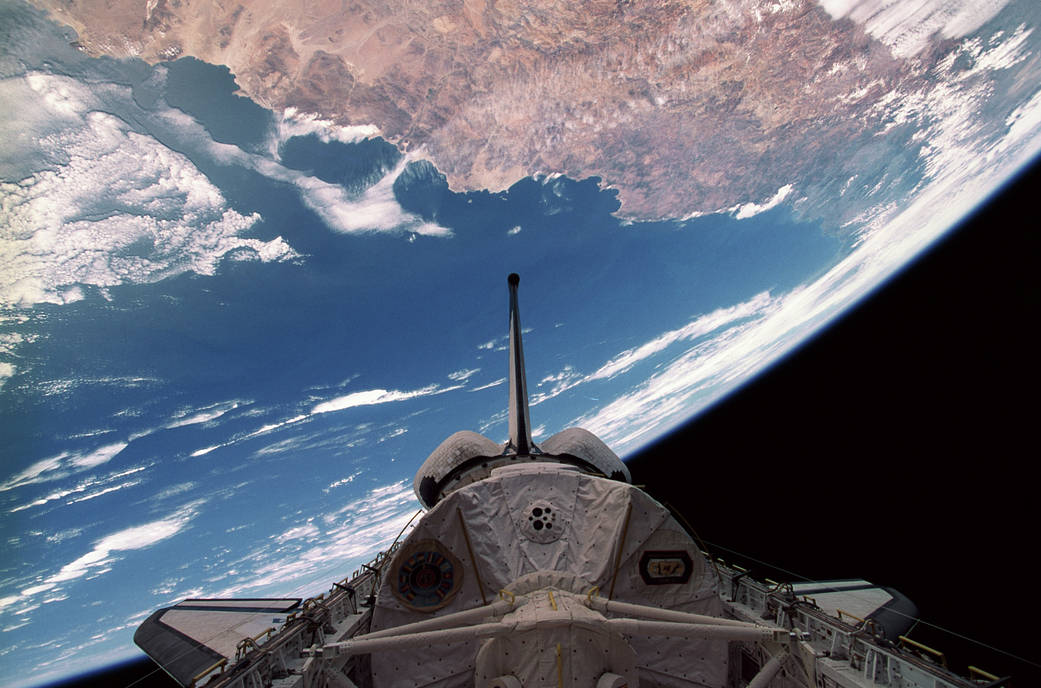 Spacelab module in cargo bay of Space Shuttle in space; the Earth is seen in the background.