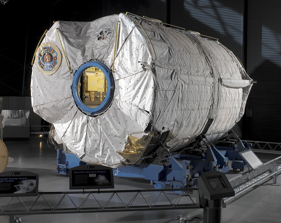 Large white cylindrical space module on display in museum setting.
