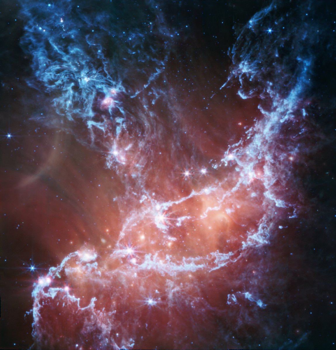 NASAWebb's tweet photo. Grim grinning ghosts 👻

Webb captured this spectral view of star-forming region NGC 346 in mid-infrared light. The blue tendrils represent silicates and sooty chemical molecules, while the red glow represents warm dust heated by bright, massive stars: https://t.co/ExyrIxSiJX https://t.co/0jyav1Du9Q