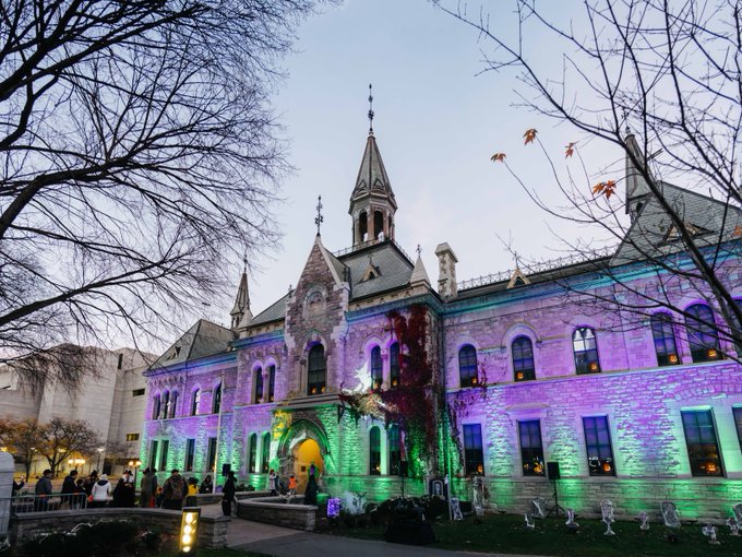 A close-up photo of the Heritage Building illuminated in purple and green with Halloween decorations outside.