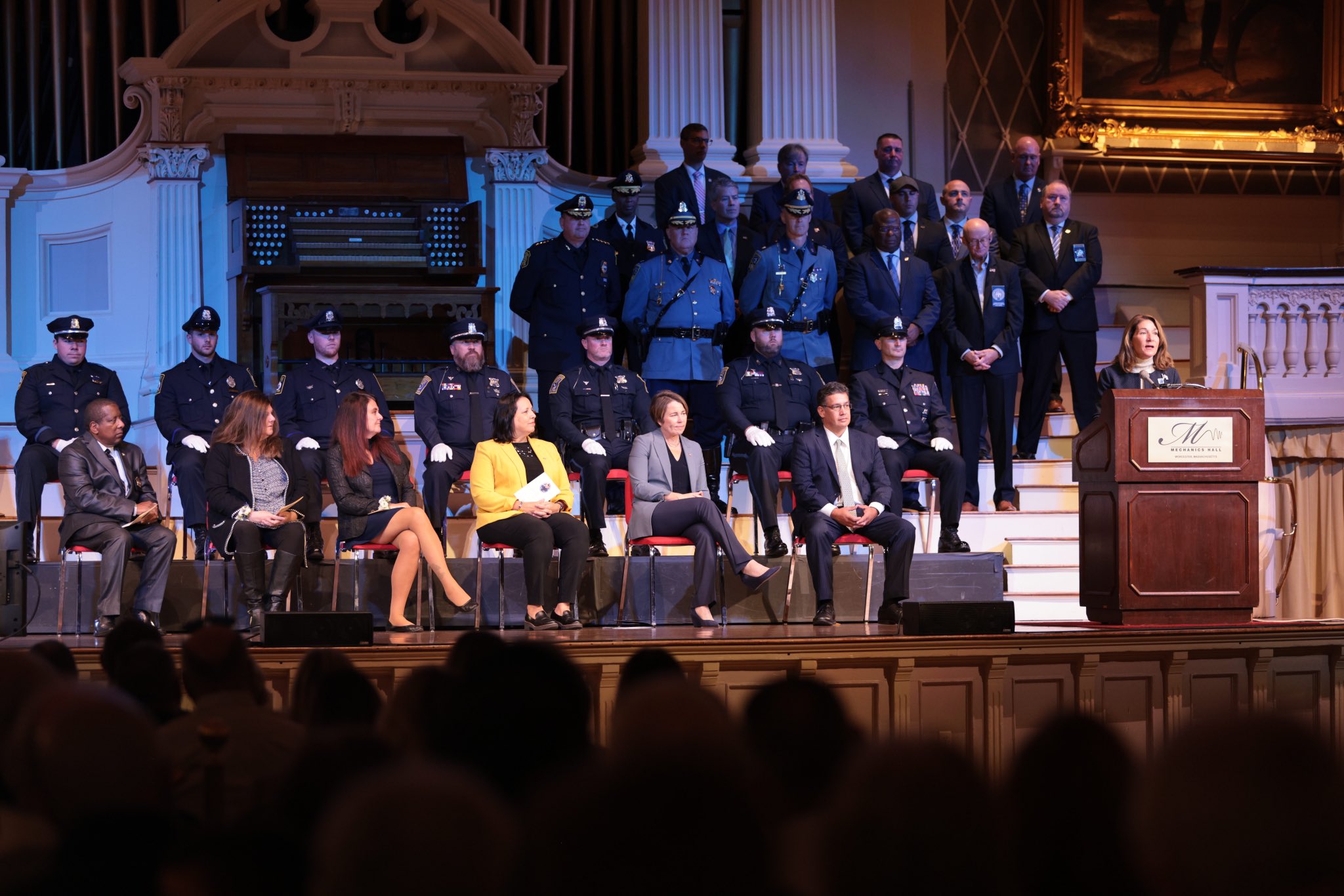 Former LG Karyn Polito at podium with other elected officials and law enforcement officers around her.