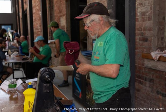 An Ottawa Tool Library volunteer in a green t-shirt and black baseball cap examines a kitchen knife.