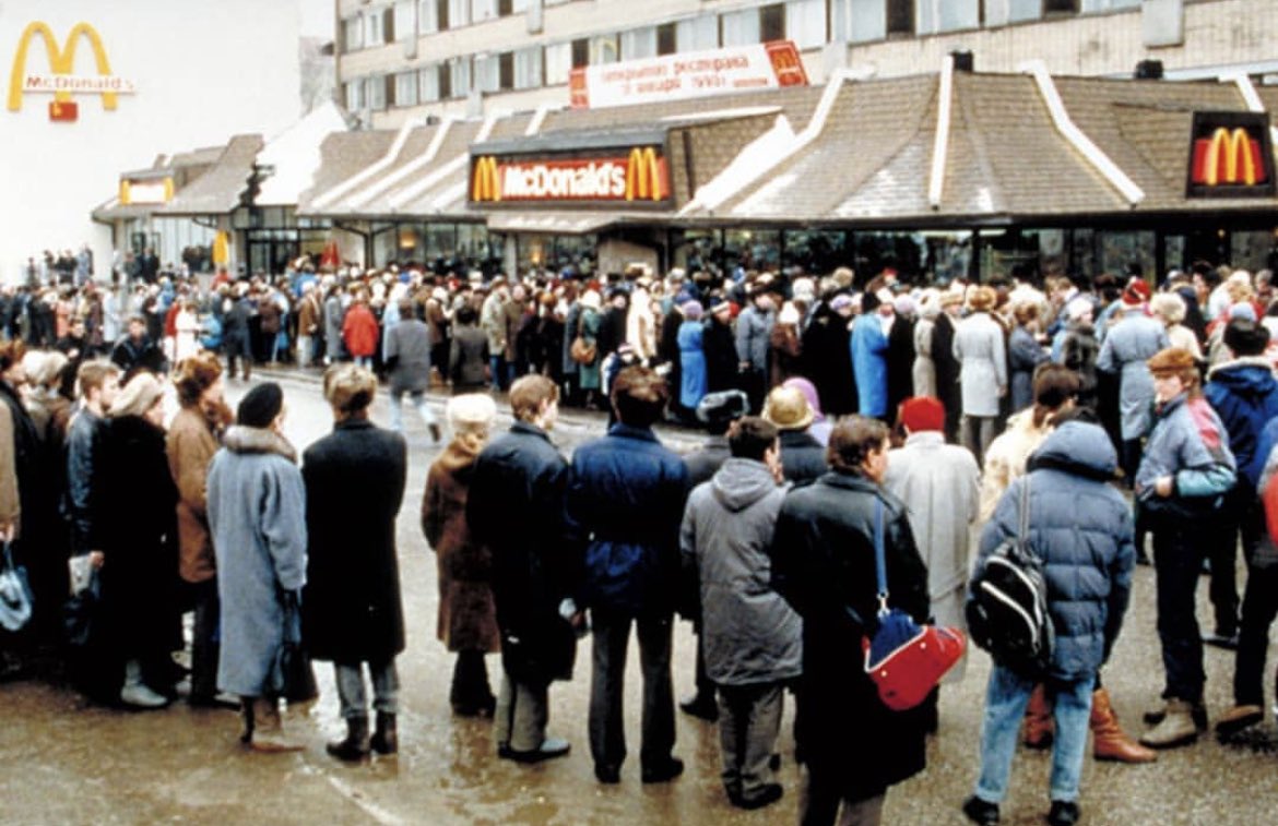historyinmemes's tweet photo. The first McDonald's in the Soviet Union opened in Moscow on January 31, 1990. At the time of its construction, the Moscow McDonald's was the largest in the world with 900 seats, run by a staff of about 600 workers who were carefully selected from 35,000 applicants. A Big Mac was selling for 3.75 rubles (equivalent to $2.34 US dollars in 1990) in a country where the average salary was 150 rubles at the time. On opening day, 5,000 Soviet citizens lined up, and approximately 30,000 customers passed through the door that day.

The lines continued to grow well into the summer months as people from other cities flocked to McDonald's. One of them was photographer Mitya Kushelevich, who gave the following account:

"We stood under the melting sun for around eight hours. That wasn't so much of a problem as we were used to standing in lines for days just to get our monthly ration of sugar and tea. Once inside, we were blown away by the number of young cashiers behind the huge counter, smiling, moving like bees, serving one meal after another. Nothing like our fat old ladies in white gowns sitting in front of empty shelves, pyramids of dusty canned food as window dressing. I still remember how insanely huge the milkshake looked, and I didn't know how to hold a Big Mac with my tiny hands.

Everything tasted more intense than anything I'd ever tried before. I ate and drank and chewed like it was my last meal on earth. Around ten minutes and 5,000 calories later, my body alerted me to the fact that it wasn't quite able to digest all the fatty deliciousness and that it was probably a good time to check out how an American toilet looked like from the inside. I wasn't alone: the queues to the toilets, especially the women's, were almost as long as the queues outside."