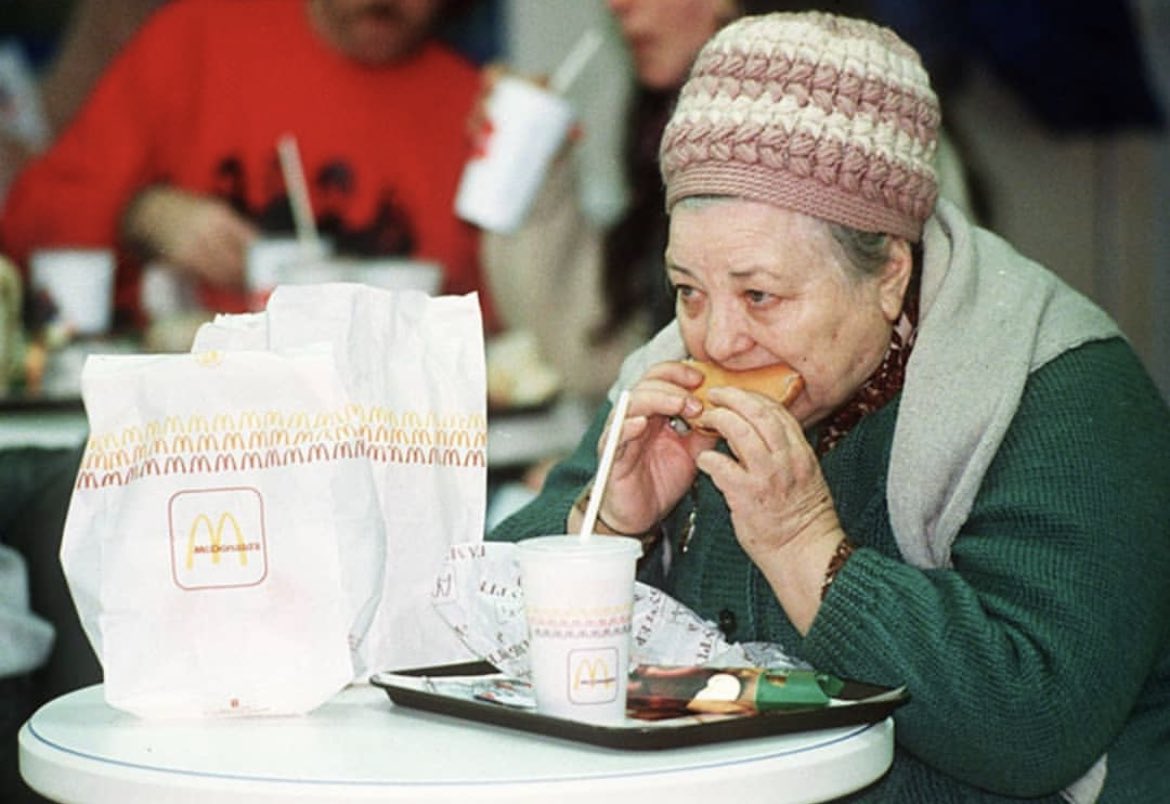 historyinmemes's tweet photo. The first McDonald's in the Soviet Union opened in Moscow on January 31, 1990. At the time of its construction, the Moscow McDonald's was the largest in the world with 900 seats, run by a staff of about 600 workers who were carefully selected from 35,000 applicants. A Big Mac was selling for 3.75 rubles (equivalent to $2.34 US dollars in 1990) in a country where the average salary was 150 rubles at the time. On opening day, 5,000 Soviet citizens lined up, and approximately 30,000 customers passed through the door that day.

The lines continued to grow well into the summer months as people from other cities flocked to McDonald's. One of them was photographer Mitya Kushelevich, who gave the following account:

"We stood under the melting sun for around eight hours. That wasn't so much of a problem as we were used to standing in lines for days just to get our monthly ration of sugar and tea. Once inside, we were blown away by the number of young cashiers behind the huge counter, smiling, moving like bees, serving one meal after another. Nothing like our fat old ladies in white gowns sitting in front of empty shelves, pyramids of dusty canned food as window dressing. I still remember how insanely huge the milkshake looked, and I didn't know how to hold a Big Mac with my tiny hands.

Everything tasted more intense than anything I'd ever tried before. I ate and drank and chewed like it was my last meal on earth. Around ten minutes and 5,000 calories later, my body alerted me to the fact that it wasn't quite able to digest all the fatty deliciousness and that it was probably a good time to check out how an American toilet looked like from the inside. I wasn't alone: the queues to the toilets, especially the women's, were almost as long as the queues outside."