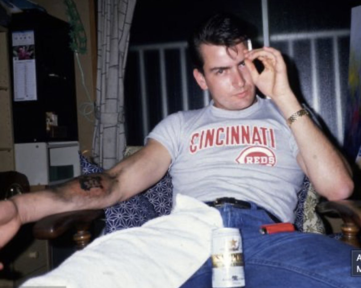 Charlie Sheen rocking a Cincinnati Reds t-shirt while smoking a dart