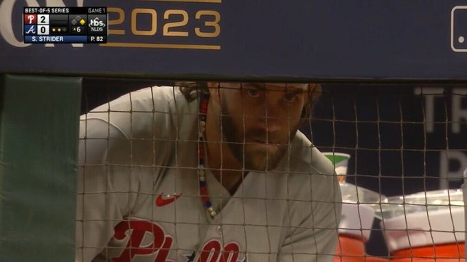 Photo of Bryce Harper staring through the netting of the dugout. His eyes looks laser like.