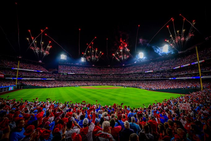 Photo of Citizens Bank Park during pregame of the NLDS Game 4. The photo is taken from the outfield. It is evening and the sky is dark. The stadium is filled with fans and there are red fireworks going off.