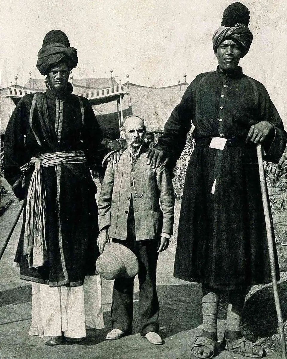 BizarreBlurbs's tweet photo. In this photograph from 1903 taken at the Delhi Durbar in British India, we see James Ricalton, an American photographer and professor renowned for his passion for travel photography, alongside two Kashmiri companions. These two friends, who were famously referred to as the "Two Kashmir Giants," served as elite riflemen under the Maharaja. One of the giants stood at an impressive height of 7 feet and 9 inches (2.36 meters), while the other measured 7 feet and 4 inches (2.23 meters).