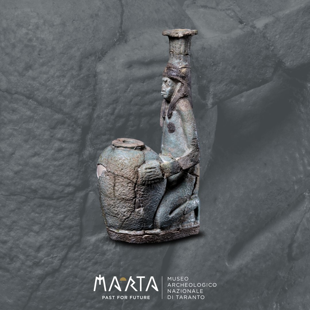 🏺 Balsamario plastico
590-580 a.C. circa
Balsamario egittizzante modellato in forma di figura maschile inginocchiata davanti a un otre, al quale si appoggia con il braccio sinistro (il destro è perduto). Sul capo un’alta palma funge da imboccatura del vasetto.