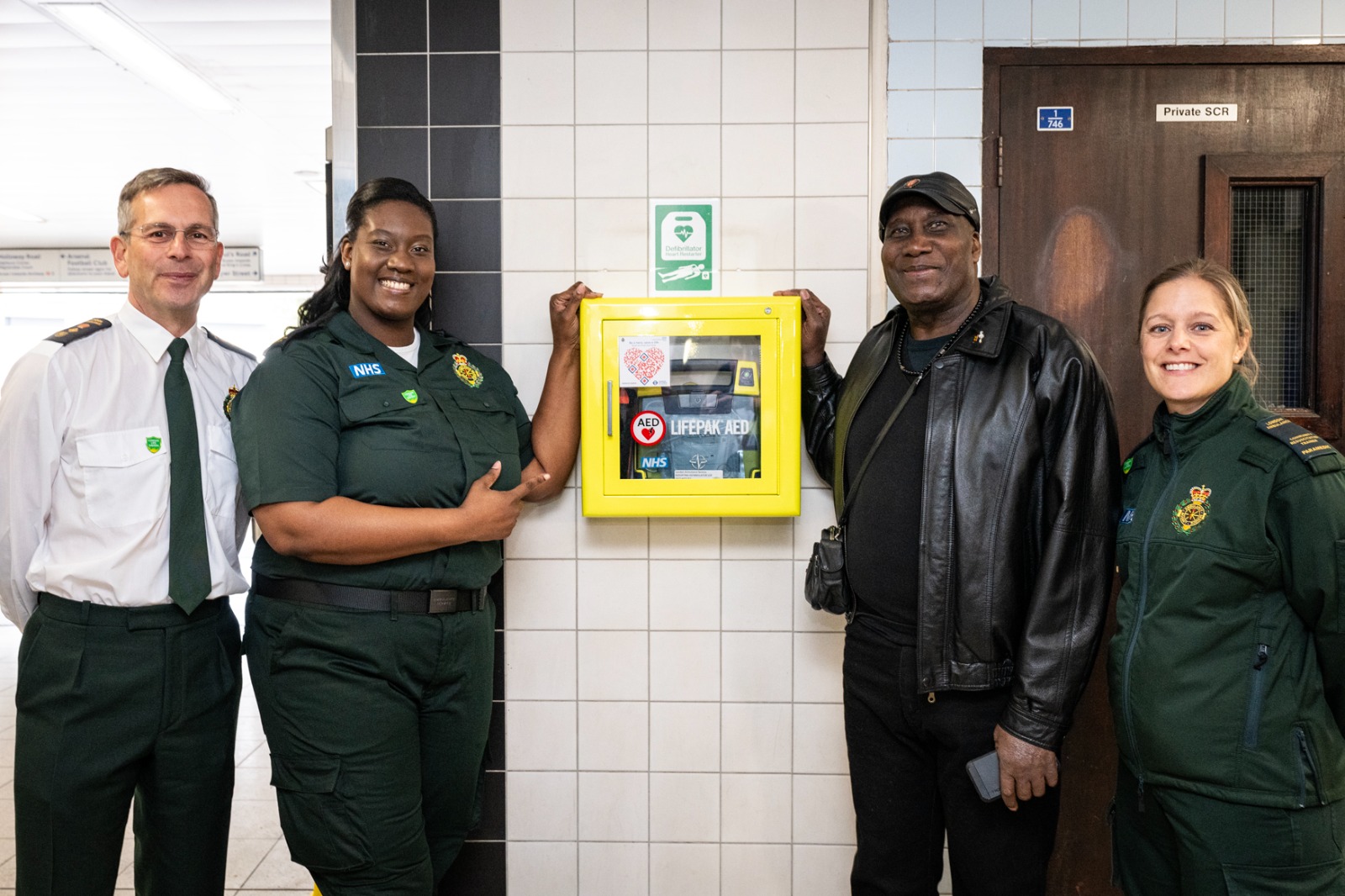 Group photo of London Ambulance colleagues standing by a newly installed defibrillator at a London underground station. 