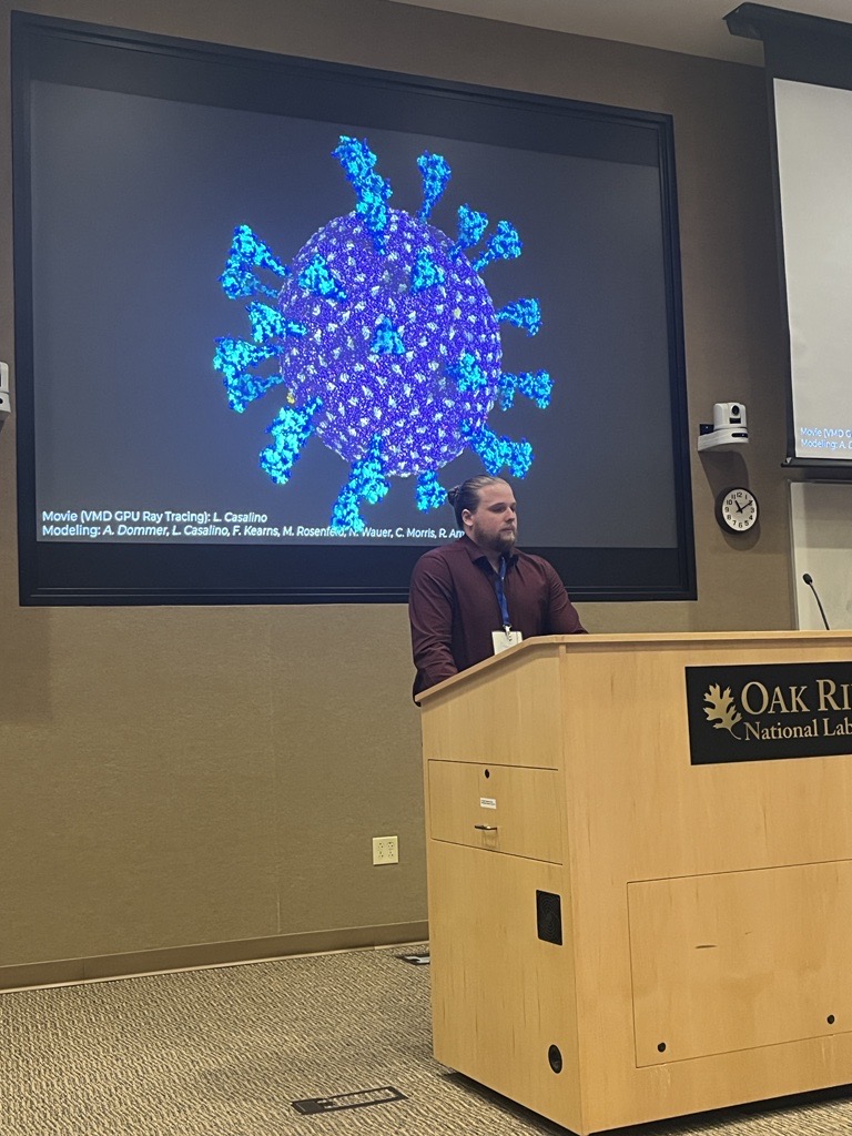 OLCFGOV's tweet photo. Nicholas Wauer from @UCSanDiego is presenting research on large-scale molecular simulations and the mechanisms behind SARS-CoV-2 aerosol transmission in his keynote talk at the 2023 OLCF User Meeting. https://t.co/x5cwAStgSc