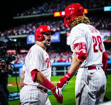 Photo of Kyle Schwarber yelling in celebrating to Alec Bohm after hitting his second home run of the game. They're wearing the red pinstripes Phillies uniform.
