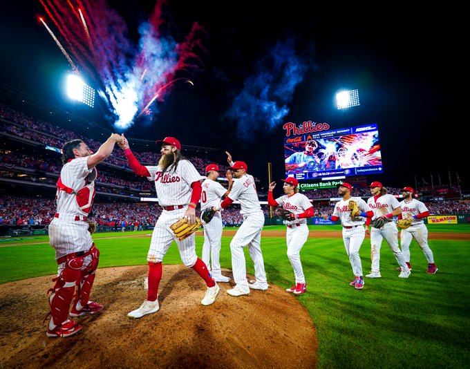 Photo of the Phillies celebrating their Game 2 win at Citizens Bank Park. They're wearing the red pinstripes Phillies uniforms. In the background, fireworks are going off and fans are cheering.