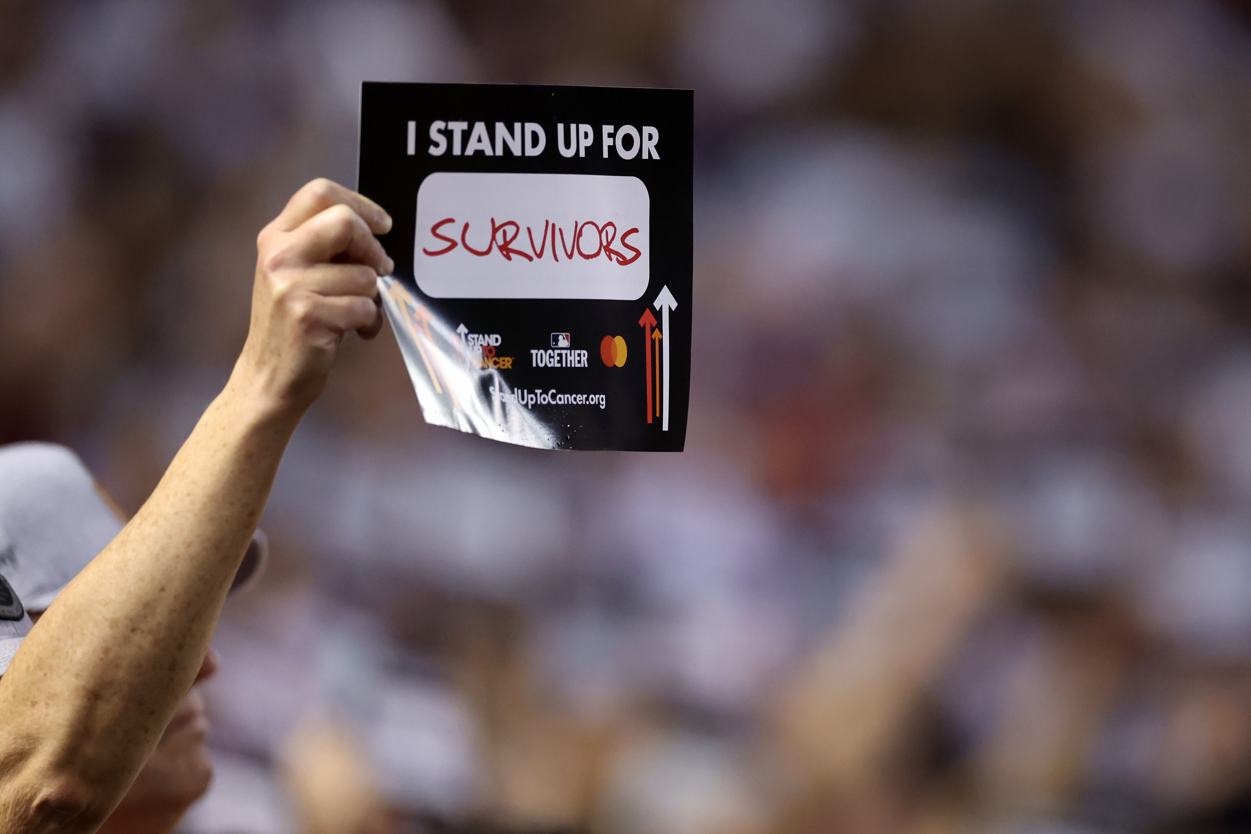 A fan holds a Stand Up to Cancer sign, "I Stand Up for Survivors."