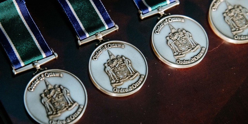 A close-up of four Order of Ottawa medals. They have a deep blue and green ribbon and include the City logo. 