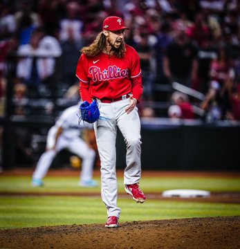 Photo of Matt Strahm celebrating in excitement after recording the final out for the Phillies to win the game. He's wearing the red Phillies jersey and grey pants.