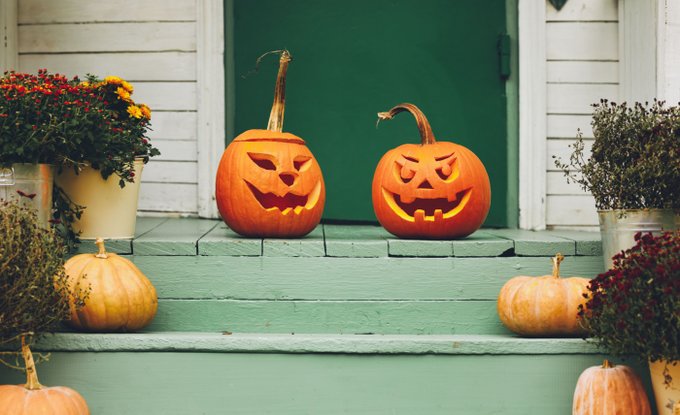 Green painted stairs leading up to a door. The steps are lined with fall planters and small uncarved pumpkins. At the top of the steps, two carved jack-o-lanterns are in the center in front of the door.