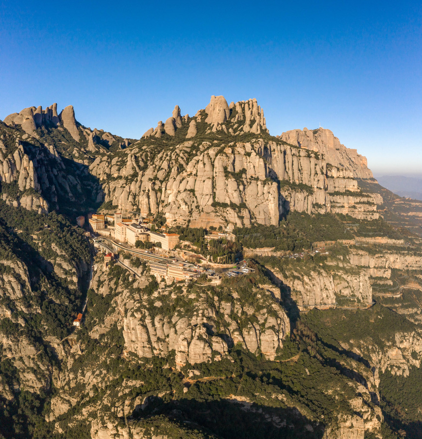 The first rays of morning gently illuminate Montserrat Monastery, revealing its grandeur against the magnificent backdrop of towering cliffs. A testament to the harmony between nature and architecture. ☀️🌲🏰 #Montserrat #Monastry #SunriseMagic #DronePhotography #NatureAndHistory