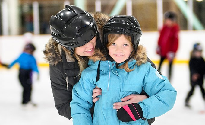 A child and an adult smile to the camera while on a skating rink.  