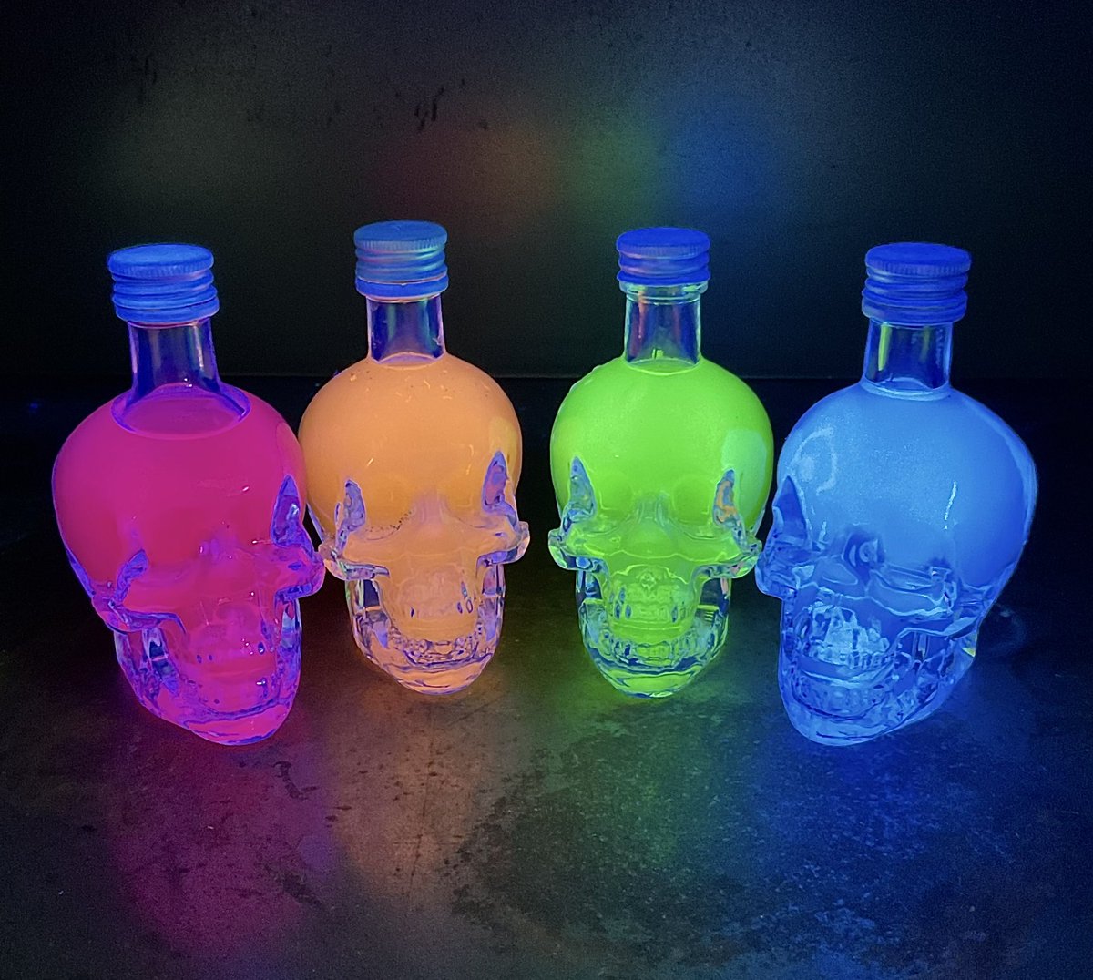 DrummerBoy2112's tweet photo. A #Halloween-themed #FluorescenceFriday photo - four colourful glowing, grinning skulls. (Skull-shaped glass bottles filled with solutions of fluorescent compounds under a UV light). #RealTimeChem #HappyHalloween https://t.co/kdB0ORp2Om