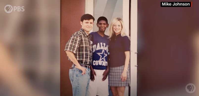 Mike Johnson's son Micheal. Presumably 40 years old in 2023. 
JOHNSON adopted Michael in 1997 when Johnson was in his mid 20s. 
I discovered this in a simple Google search and a bit of research. 
Picture taken from a documentary produced by PBS in 2020.