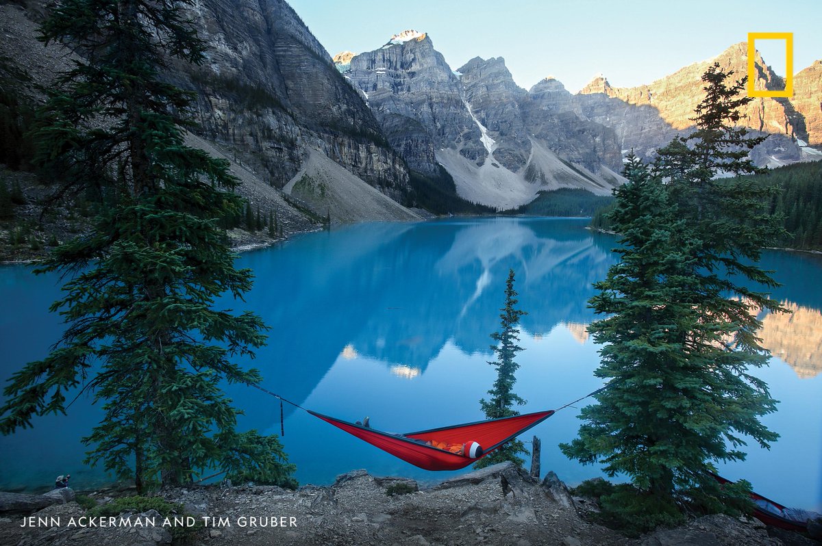 A tourist lies in a hammock as the sun rises on Moraine Lake and the Valley of the Ten Peaks in Banff National Park, Canada.