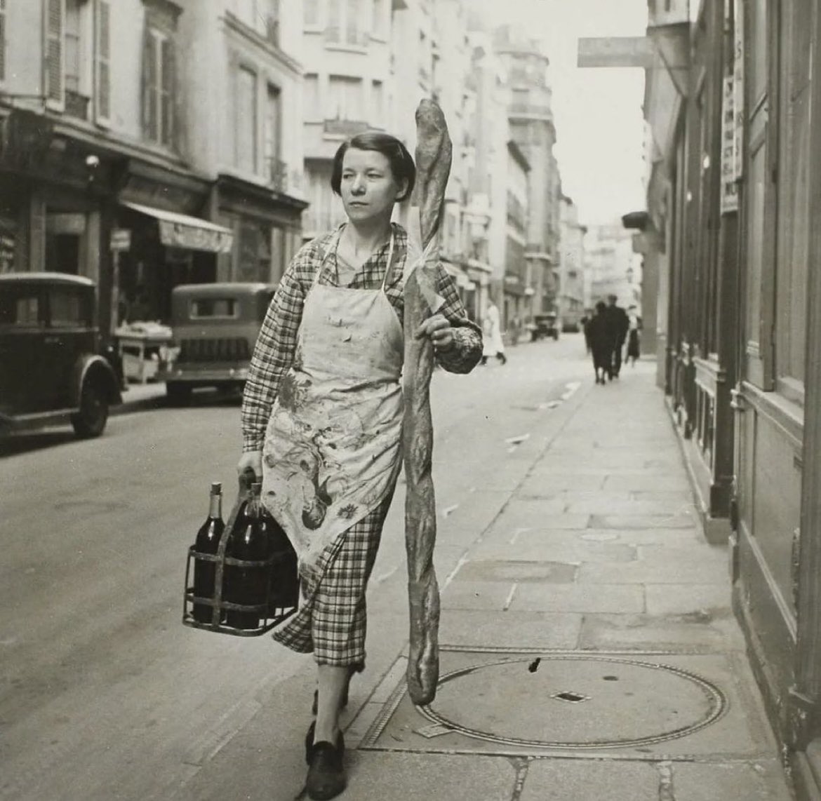 A French woman walks the streets of Paris France with her baguette and six bottles of wine, 1945.
