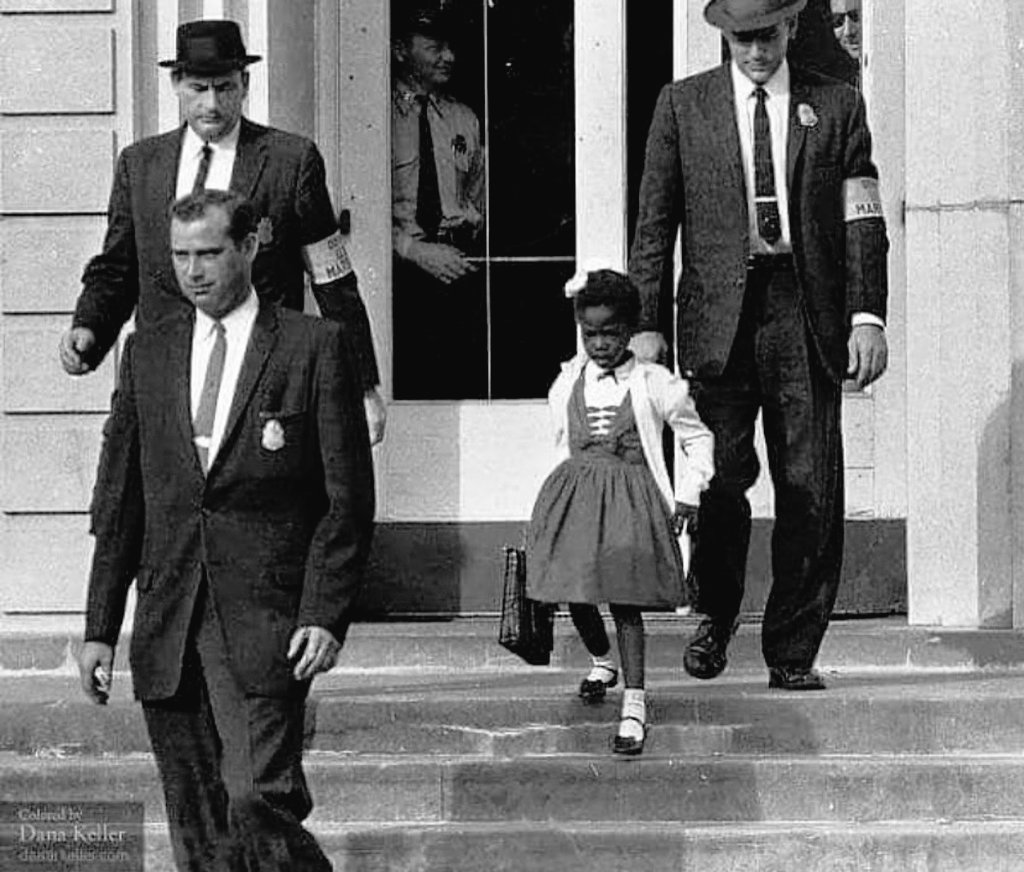 RelatocuriosoK's tweet photo. La niña Ruby Bridges, con sólo 6 años, es escoltada por delegados federales en Louisiana, 14 de noviembre de 1960. Bridges fue la primer estudiante negra estudiando en una escuela para blancos, ella participó en un proyecto federal que pretendía acabar con la segregación racial en las escuelas del estado de Louisiana.

El 14 de noviembre de 1960, Ruby bridges se dirigió a la escuela William Franz en Nueva Orleans. Tomó coraje, entró a las dependencias del colegio y se encontró con la institución vacía.

El cuerpo docente se había negado a enseñar a la niña negra y los padres del resto de las/los estudiantes no los llevaron más a esa clase. Sólo una maestra se ofreció a enseñarle y lo hizo todo ese año, como si tuviera la presencia de más estudiantes en la sala.

Al final del primer día de clase, tres alguaciles federales, armados, esperaban a la gran Ruby para escoltarla a casa, frente a una multitud de casi 1000 personas que la agredían verbalmente, la escupían y la amenazaban de muerte. El Delegado federal Charles Burks, recordó más tarde: "ella mostró mucha valentía, nunca lloró. Ella no lloró. Sólo marchaba como un pequeño soldado, y todos estamos muy orgullosos de ella...".