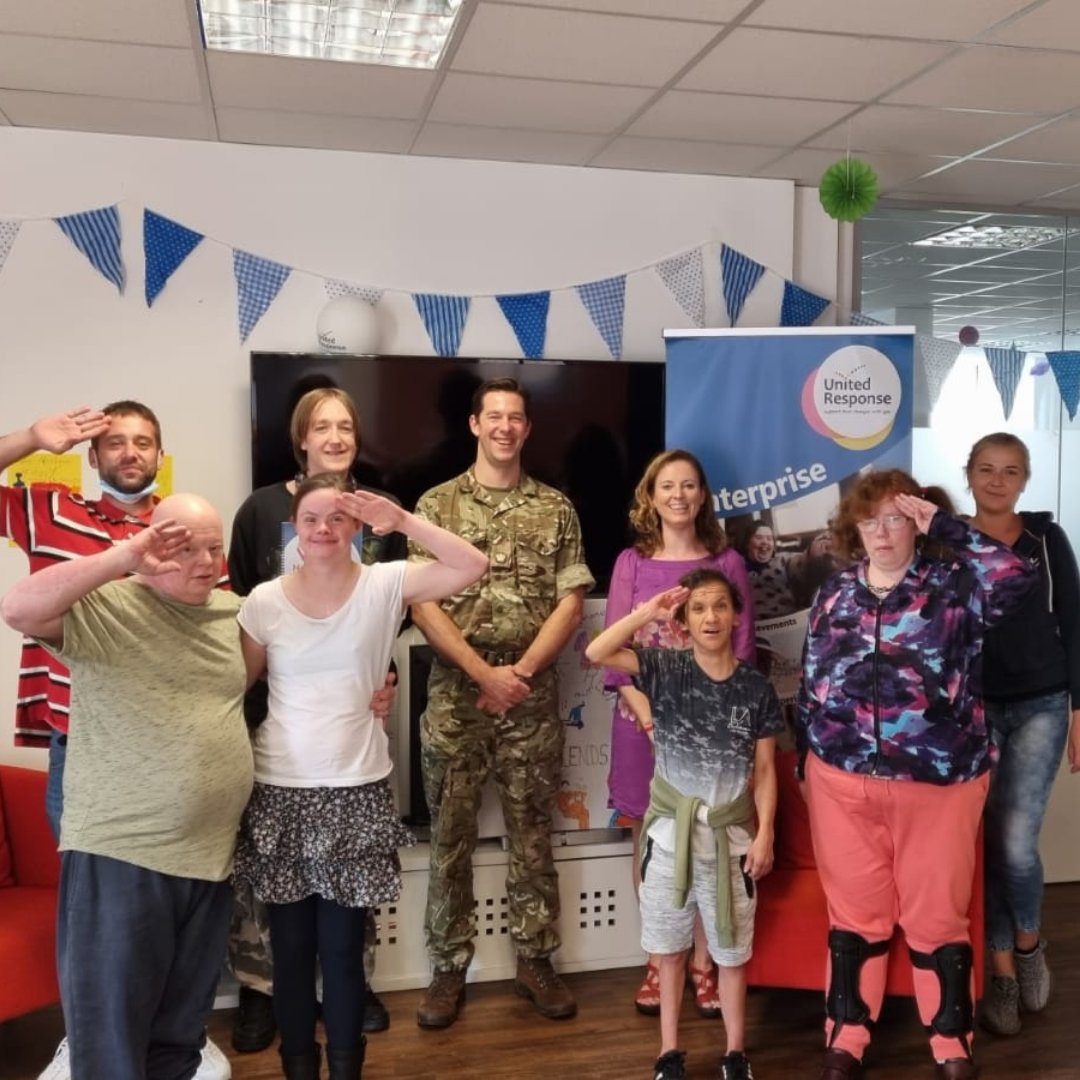 Staff and people we support in our Wellbeing group at The Enterprise are stood around soldier Tom who is wearing camouflage. Some of the group are doing a salute.