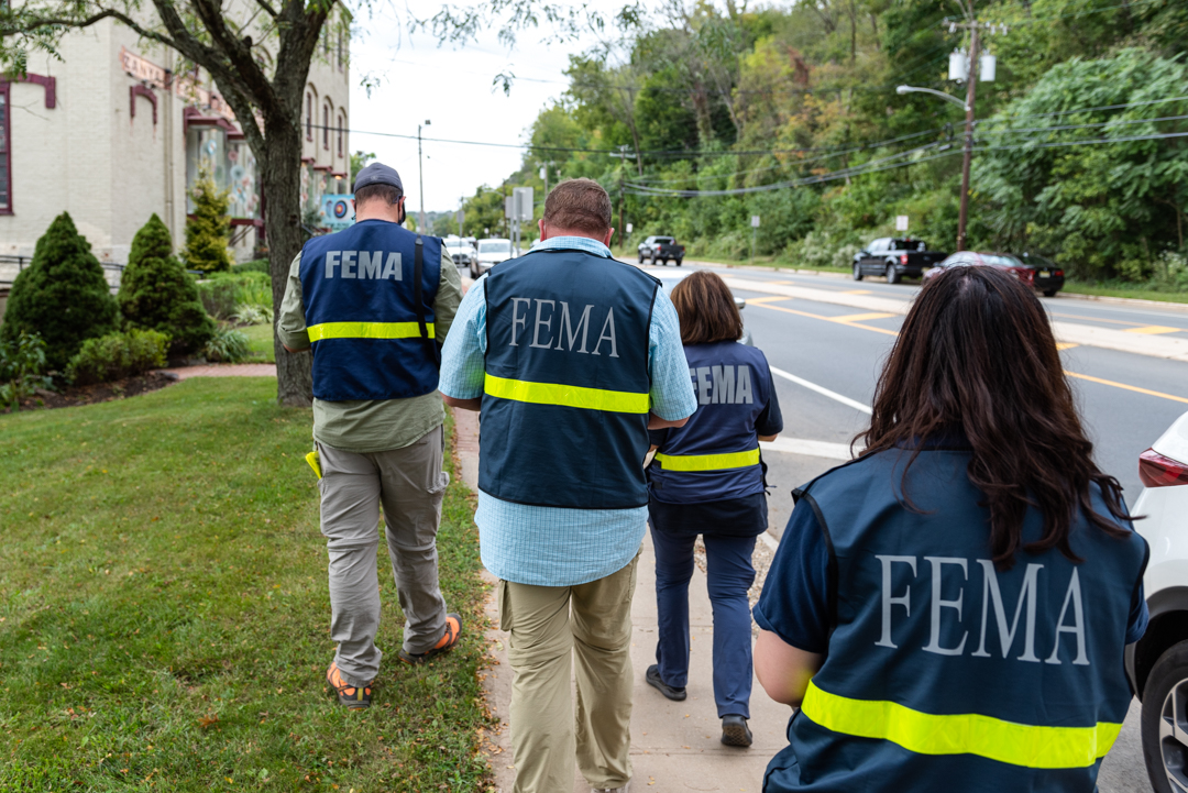 Four people in FEMA jackets walking down a street with their backs to the camera.