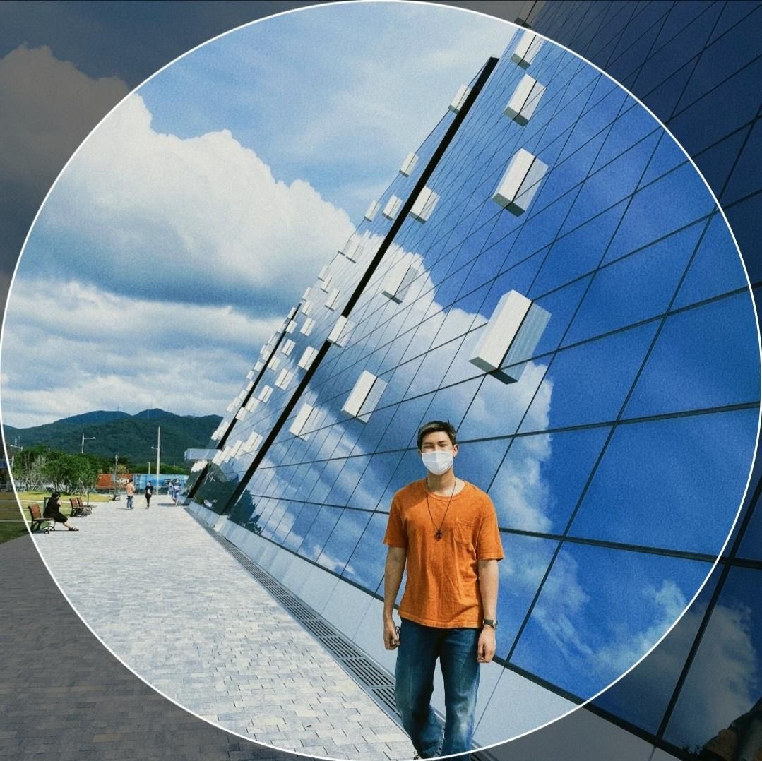 namjoon’s weverse profile picture, standing in front of a reflective building of mirrors with an orange tee!