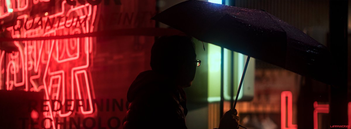 Photography by Liam Wong of Tokyo at night. A man walks by a red neon sign holding an umbrella. 