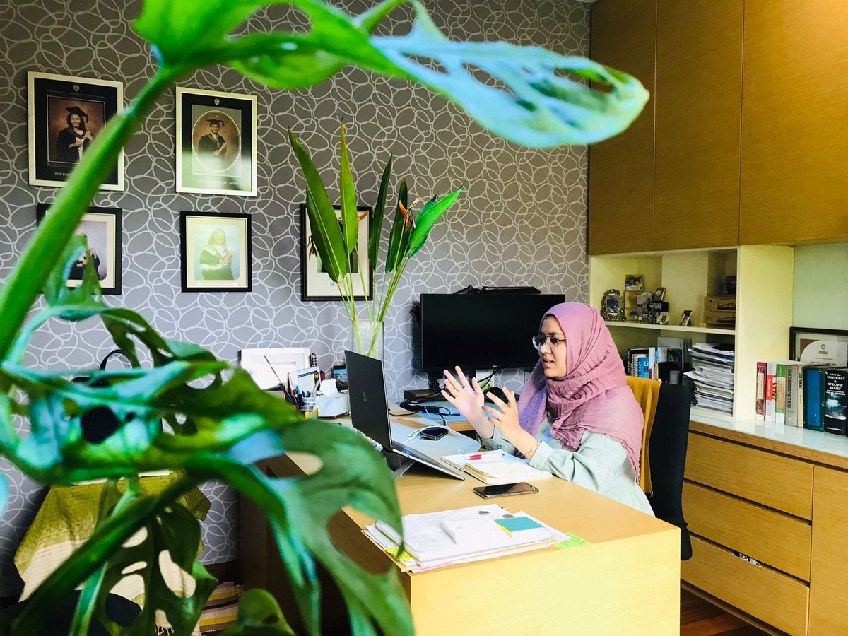 Female in hijab speaking with open hands to computer screen in an office