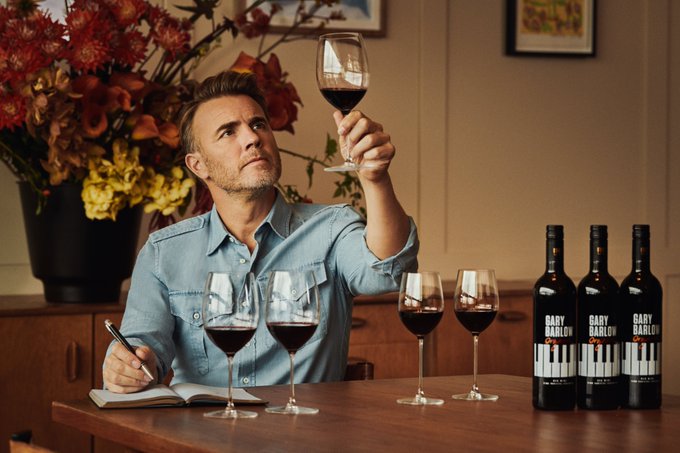 Gary Barlow, dead serious, looking at a glass of wine from his new wine brand