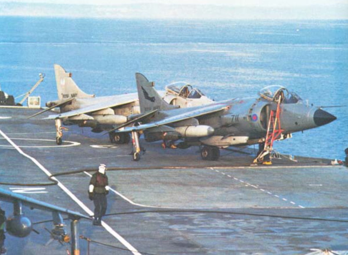 HarrierPres's tweet photo. Shown here not long after the end of the Falklands, ZE690 from 899NAS and a 809NAS aircraft (not sure to its identity) sit on the deck of HMS Hermes. Note the CBLS fitted to each aircraft, and the odd coloured gunpod of 690. #809NAS #899NAS #Harrierpres #SeaharrierFRS1 #HMSHermes https://t.co/IqiepkSBNZ