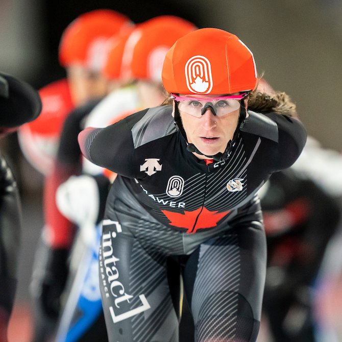 A close up of Ivanie Blondin competing in the mass start event. Behind her, out-of-focus are other racers.
