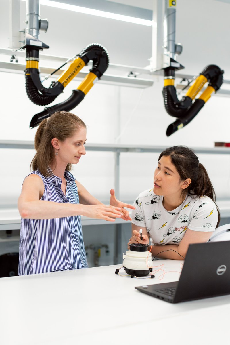 Women communicating in lab, robot and laptop on table in front of them. 