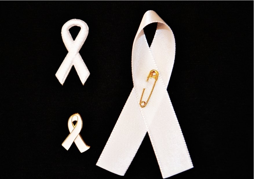 Three images of white ribbons available to purchase from the White Ribbon online shop. One is a literal White ribbon held with a small gold safety pin, another is a pin badge with gold edging around the White enamel the third is a white ribbon that's more quilted.