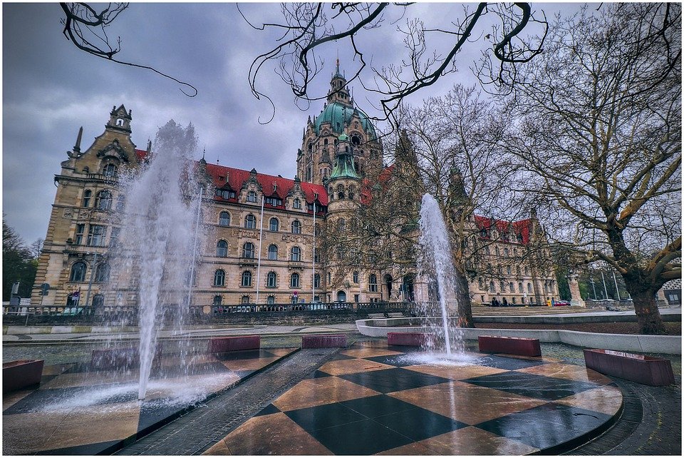 Rathaus Hannover, im Vordergrund zwei Wasserfontänen. Rechts Geäst eines Baums.